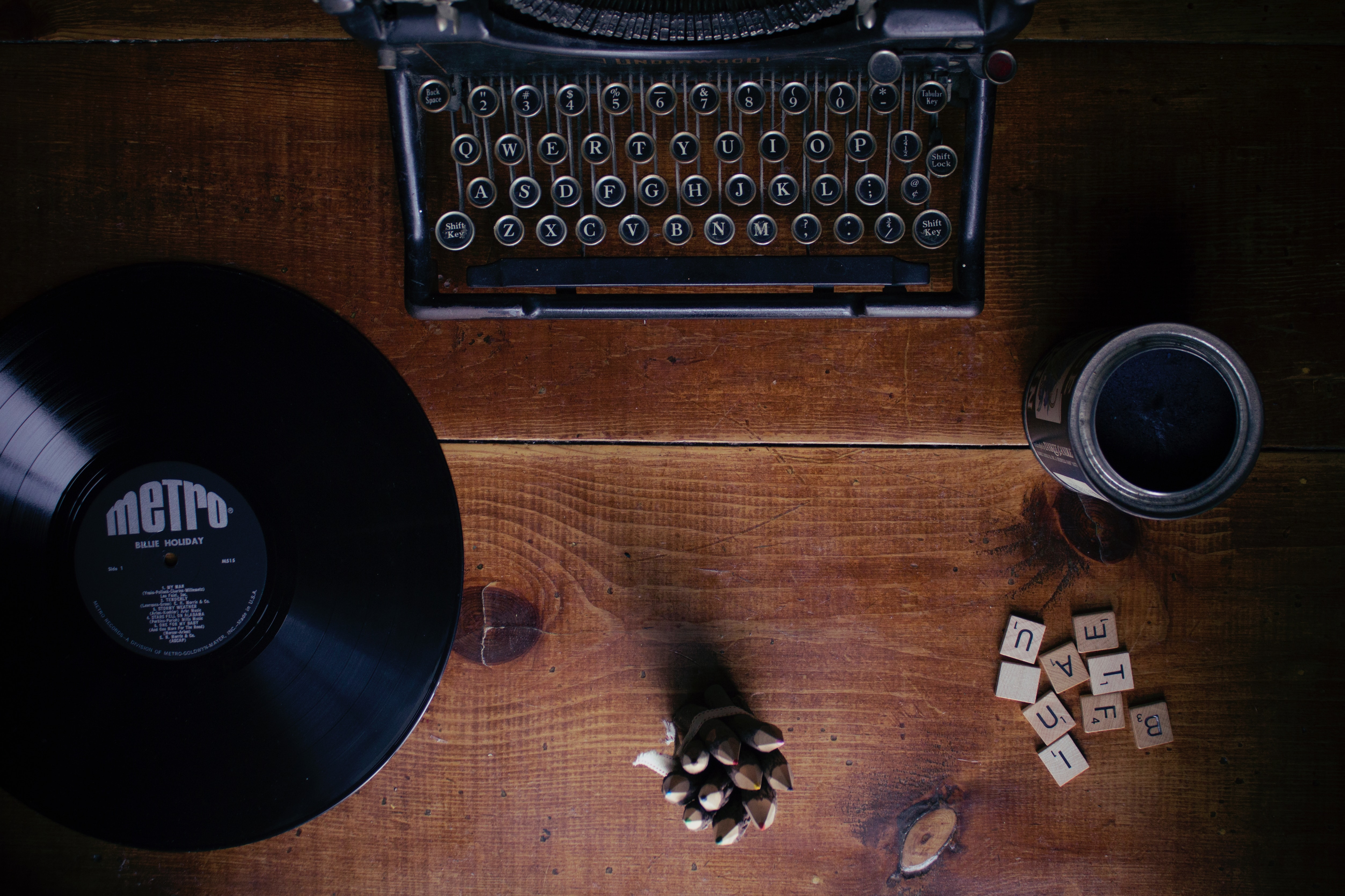a desk with a record, a typewirter, a cup, a pinecone, and Scrabble tiles sitting on top